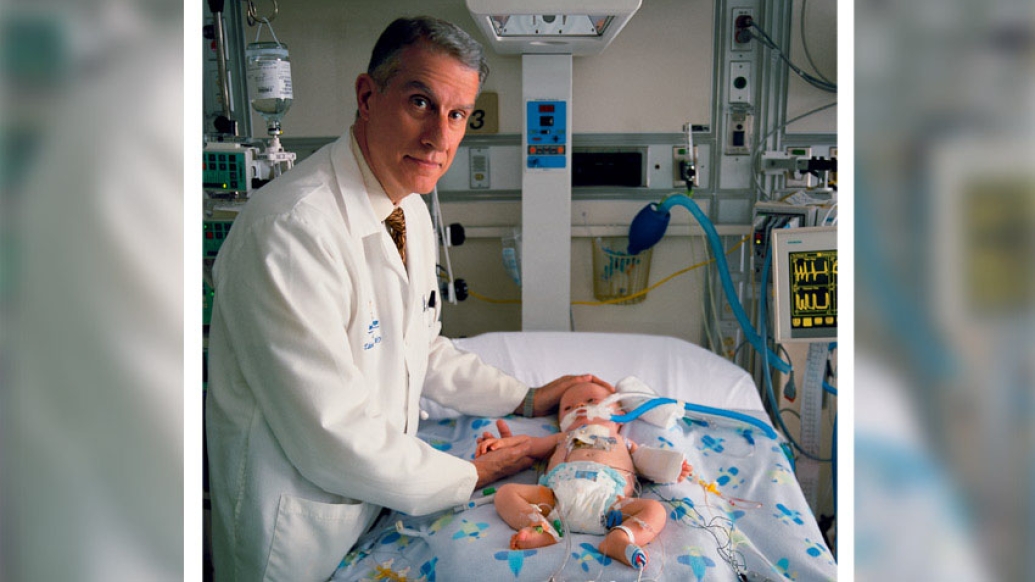 Doctor smiling by bed near baby with tubes