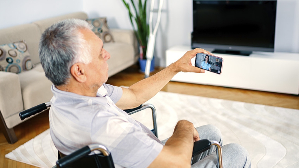 man in wheel chair talking to doctor on smart phone in living room