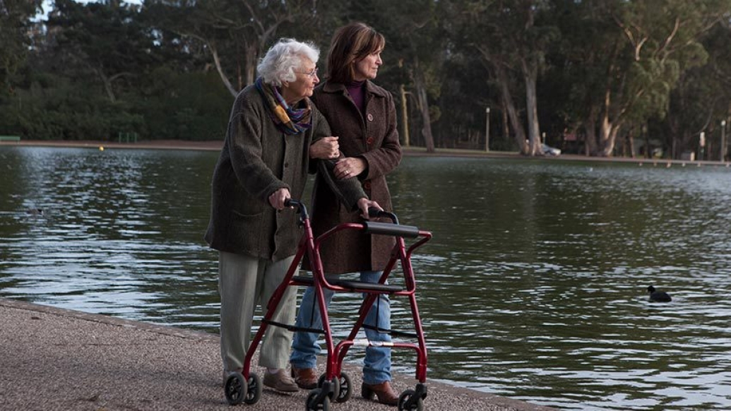 senior woman walking with walker with woman by pond