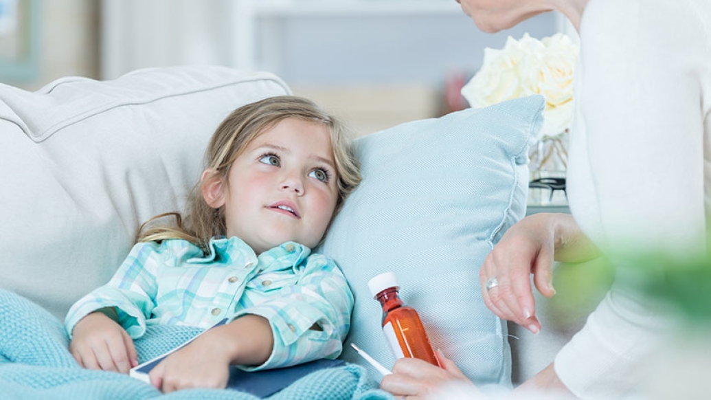 Little girl in bed with a woman next to her with a bottle of medicine in her hand
