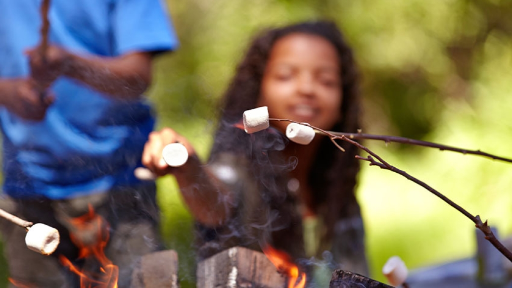 child holding stick of marshmallows over camp fire
