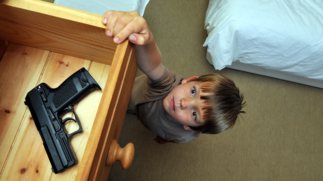 Child reaching for a gun laying in an open drawer