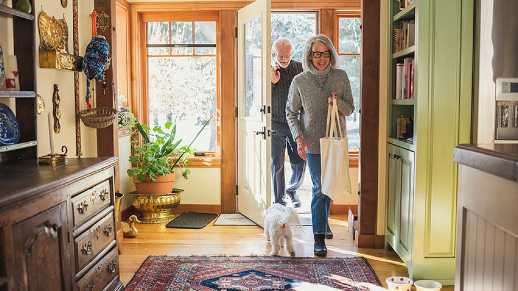 Older couple entering into home with bags of groceries.