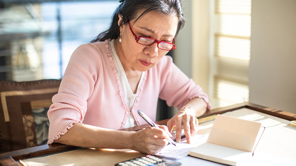 woman doing bills in living room with pink shirt and red glasses on